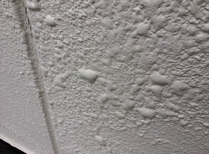 下塗り材の選定を誤ったことで、外壁の塗膜表面に膨れや不均一な凹凸が出ている状態を示した画像